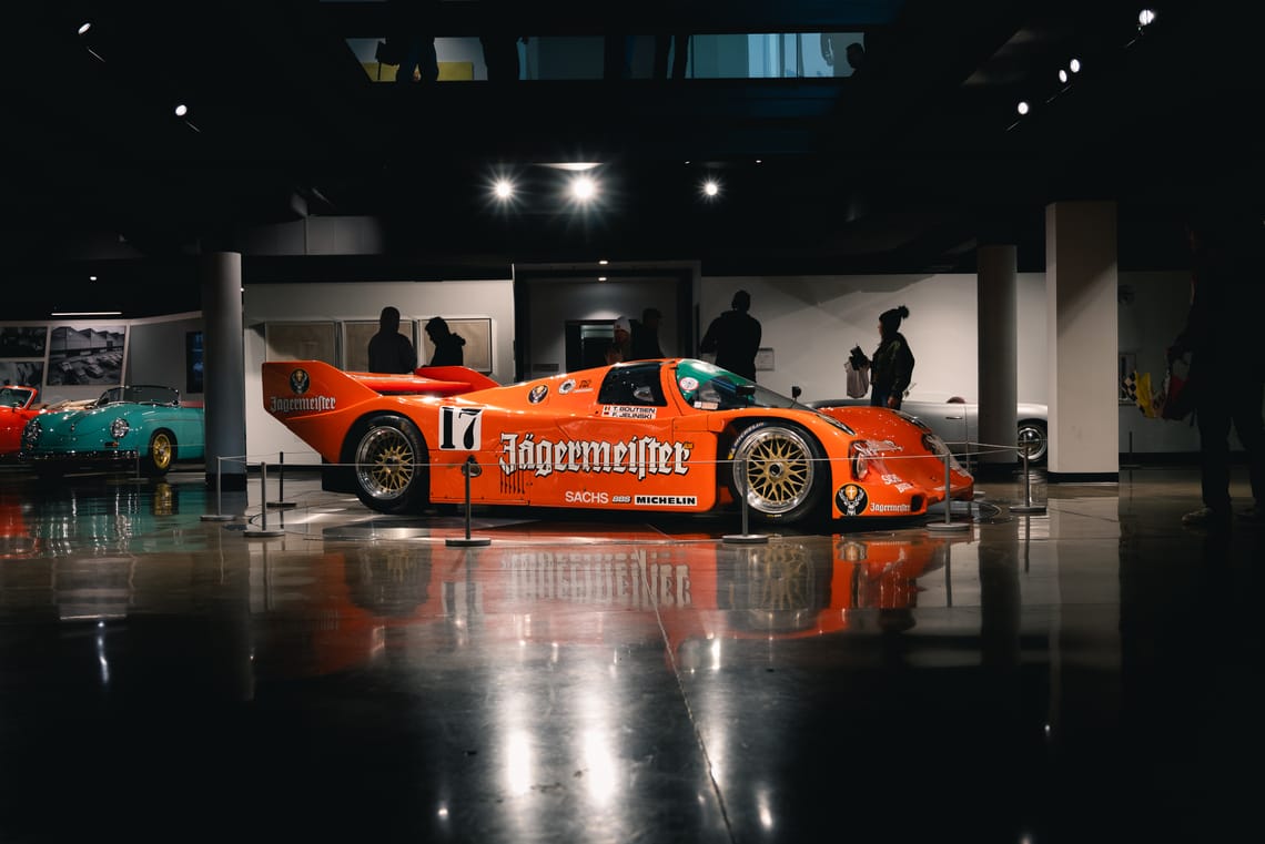 Porsche 962 with a Jägermeister livery on the showroom floor at a Porsche dealership in Santa Clarita